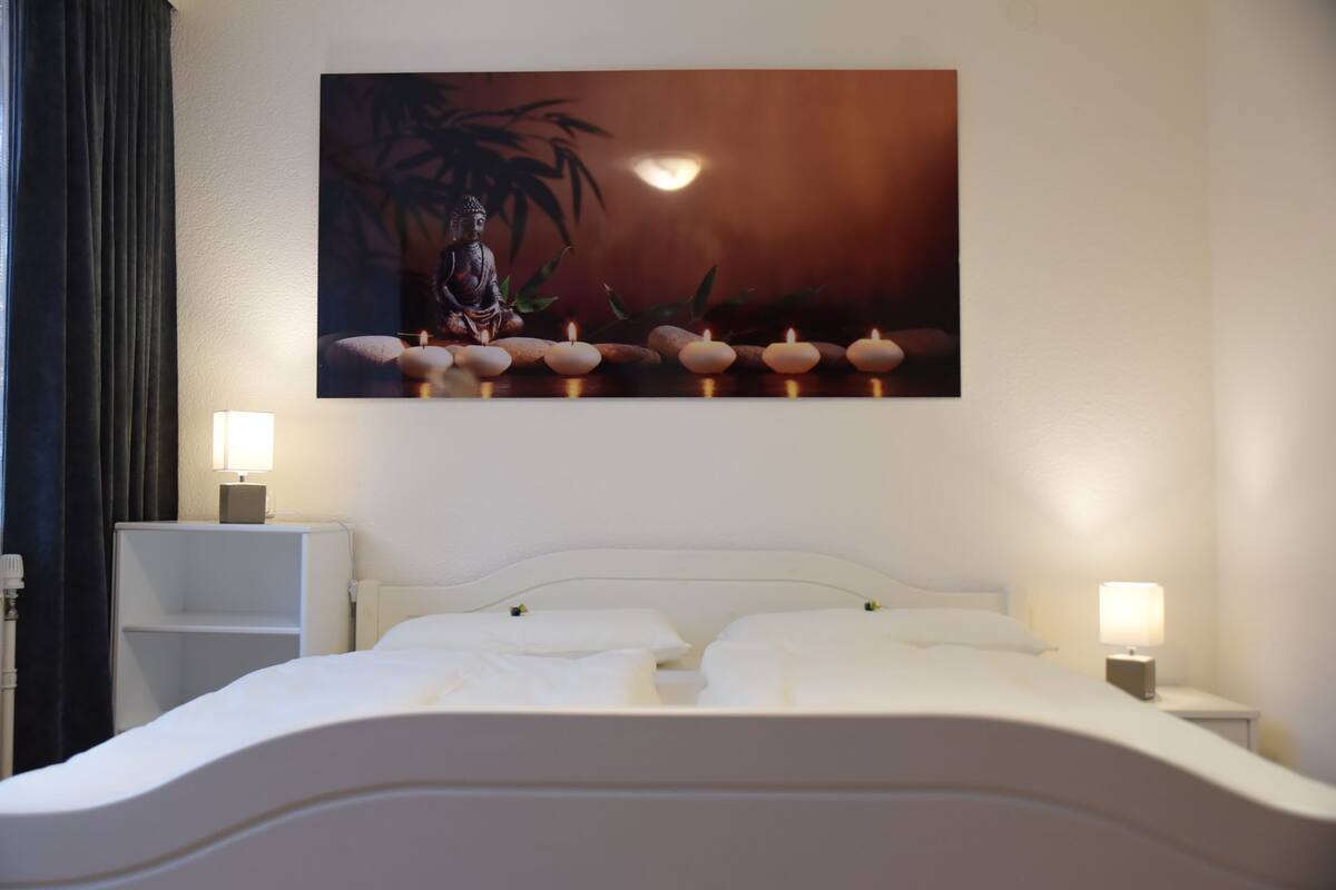 A neatly made bed with white linens, a headboard, and two bedside tables with lamps.