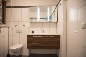 A modern bathroom with a white toilet, a wooden vanity with a mirror, and a wall-mounted sink.