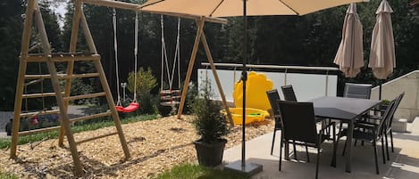 A patio with a swing set, a table with chairs, and a large umbrella.