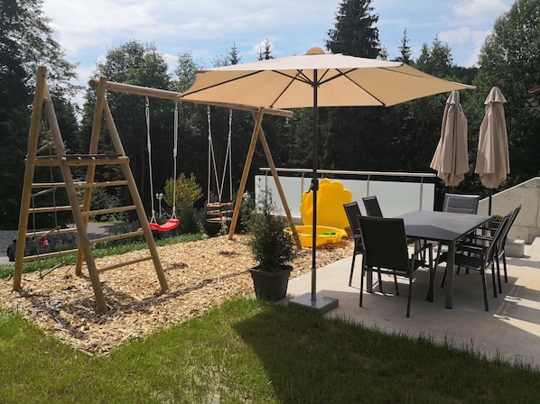 A patio with a swing set, a table with chairs, and a large umbrella.
