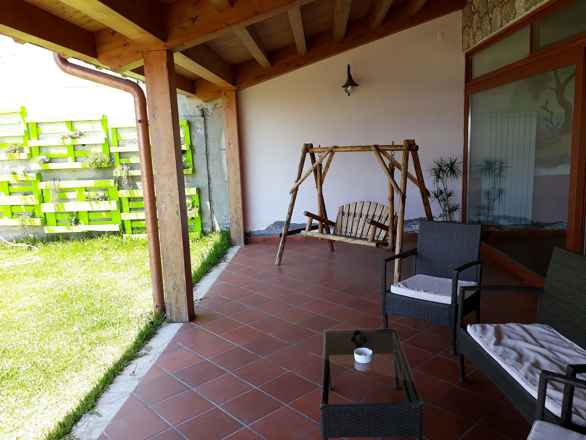 Une terrasse couverte avec une balançoire, des meubles en osier et un sol carrelé.