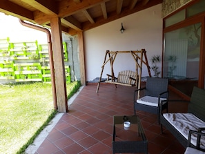 Un patio cubierto con una hamaca, muebles de mimbre y suelo de baldosas.