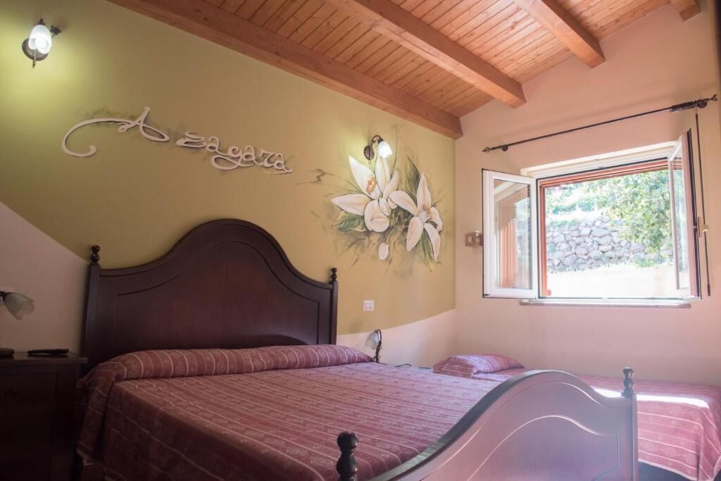 Une chambre avec un plafond en bois, un lit avec une tête de lit, un mur orné d’une fresque florale et une fenêtre avec des rideaux.