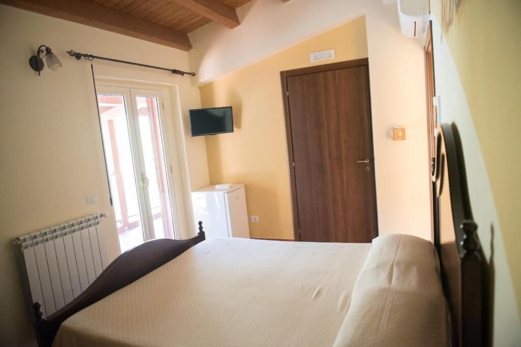 A bedroom with a bed, a television mounted on the wall, a wooden door, and a radiator.