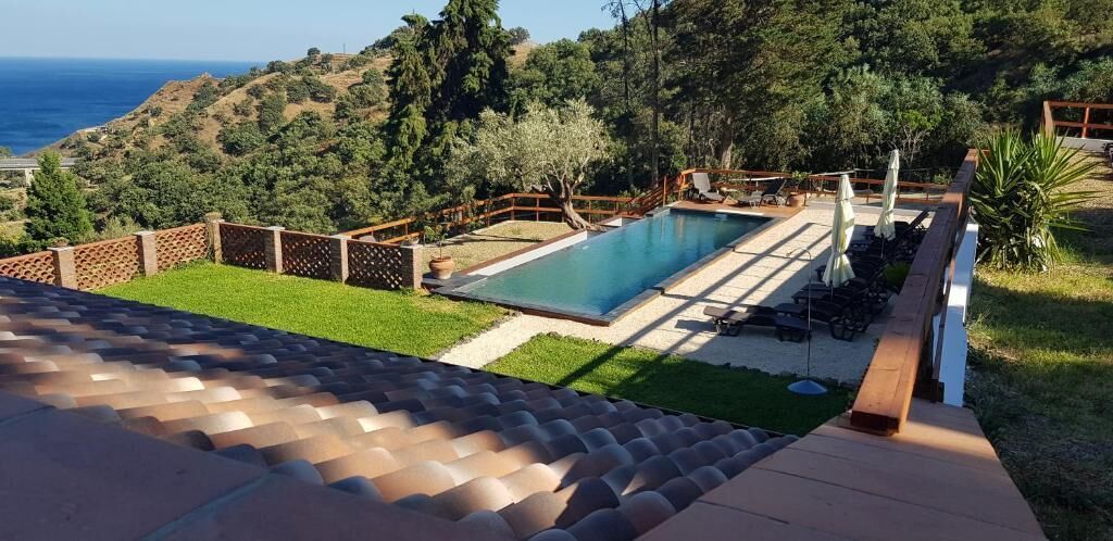 A swimming pool with a wooden deck, surrounded by a fence and a view of the ocean.