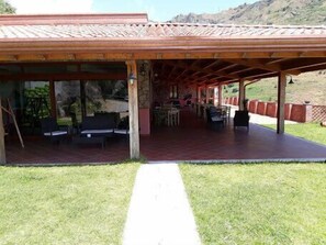 A covered outdoor area with seating and tables, surrounded by a stone wall and a mountain backdrop. - Valle Lumia (Gallodoro)