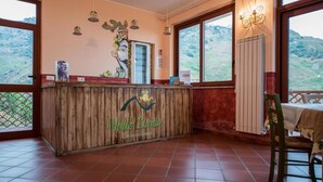 Zona de recepción con mostrador de madera, vista al exterior y una mesa con una silla.