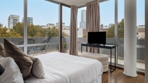 A modern hotel room with a large bed, a TV, and a balcony with a city view. - Nido x Palermo Soho Square (Buenos Aires)