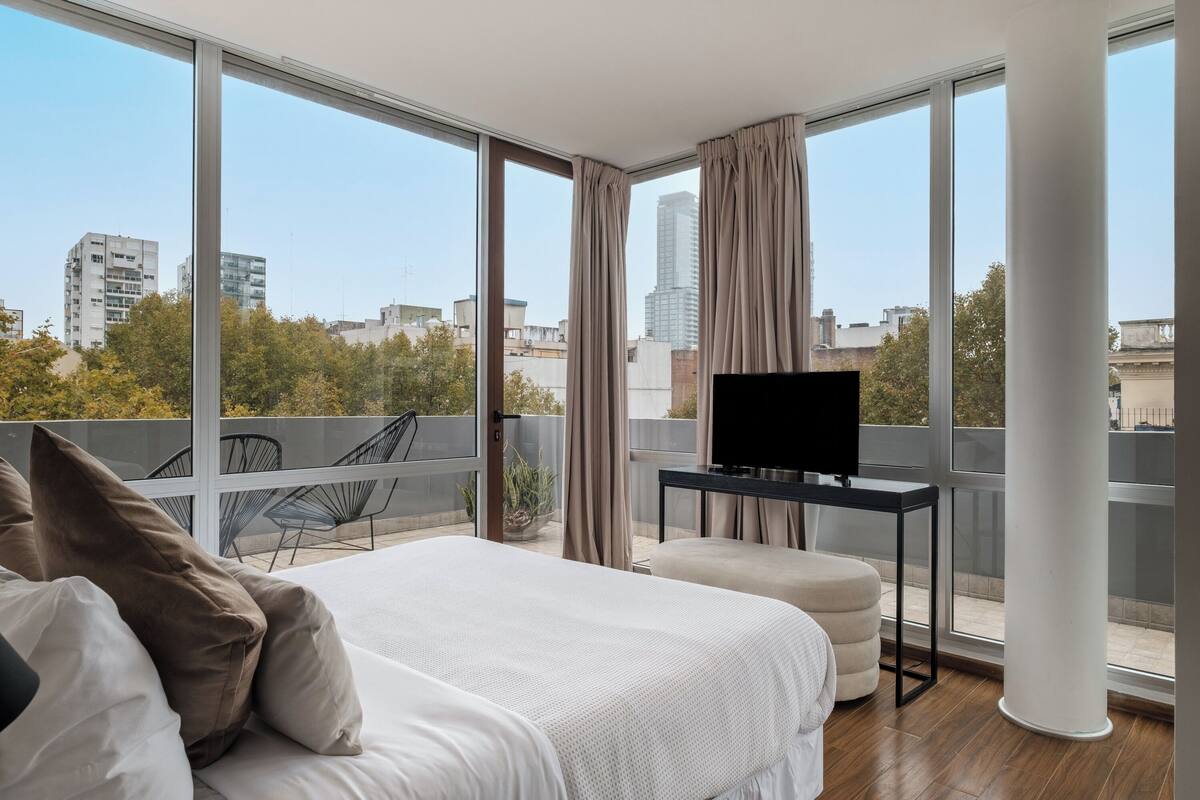 A modern hotel room with a large bed, a TV, and a balcony with a city view.