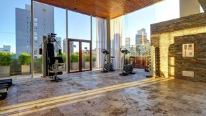A modern gym with exercise equipment, large windows, and a stone wall. - Nido x Palermo Soho Square (Buenos Aires)