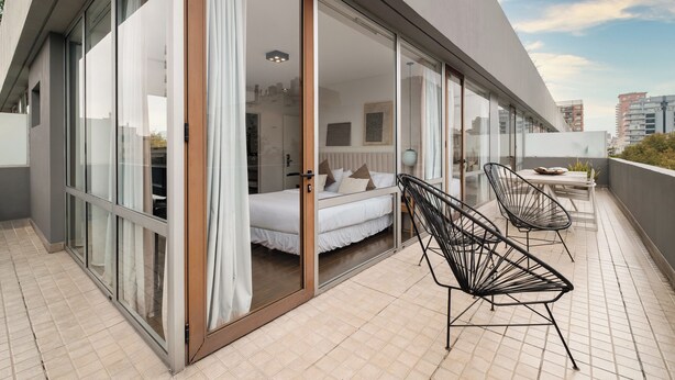 A modern hotel room with a large sliding glass door leading to a balcony with two black wireframe chairs and a small table. - Nido x Palermo Soho Square (Buenos Aires)