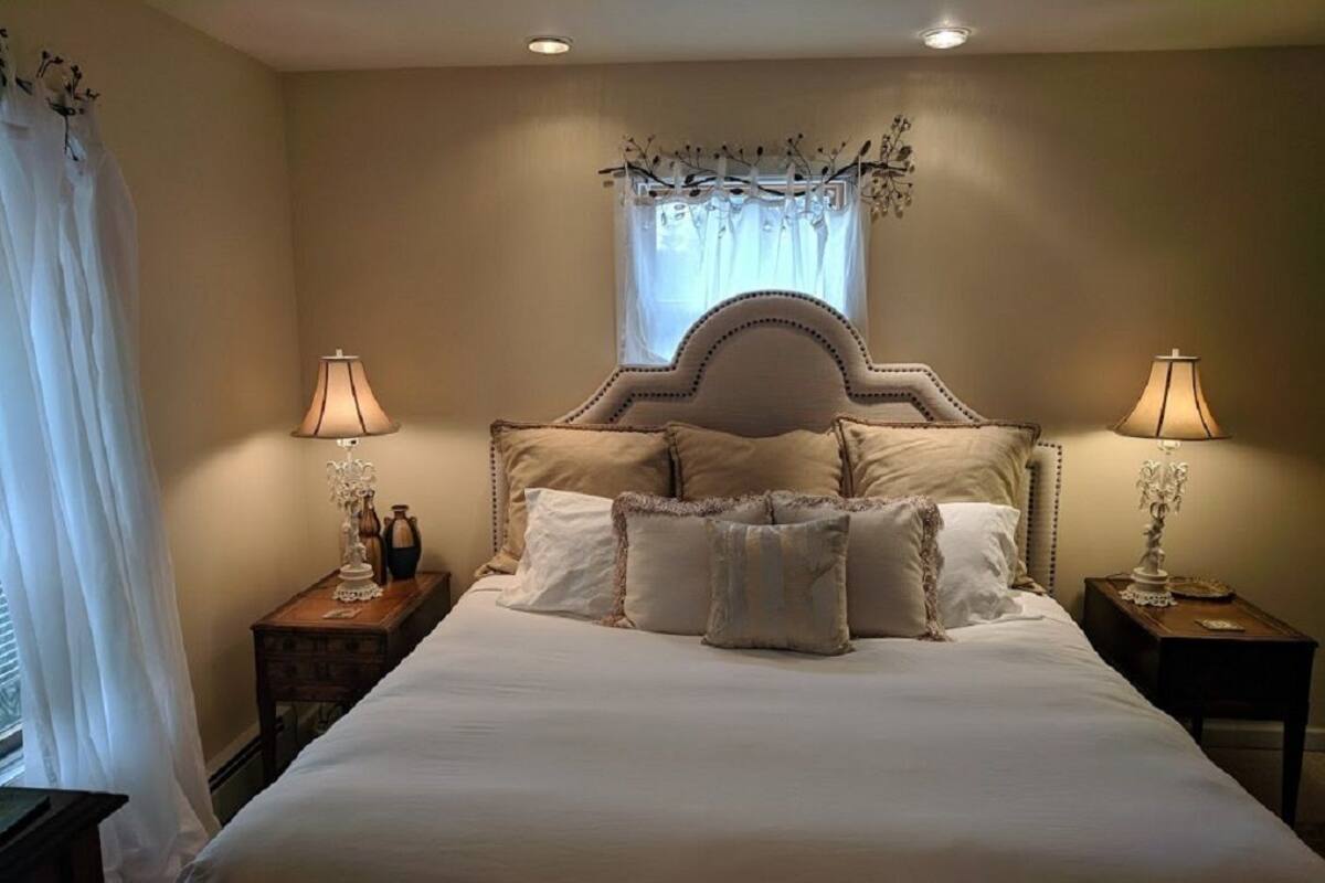 A neatly made bed with a headboard, two bedside tables with lamps, and a window with sheer curtains.