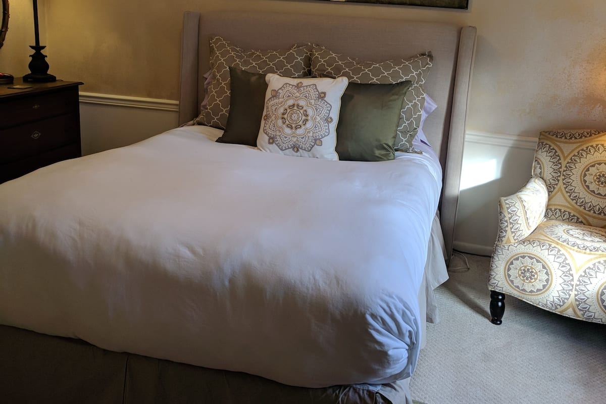 A neatly arranged bedroom with a bed, a chair, a lamp, and a ceiling fan.