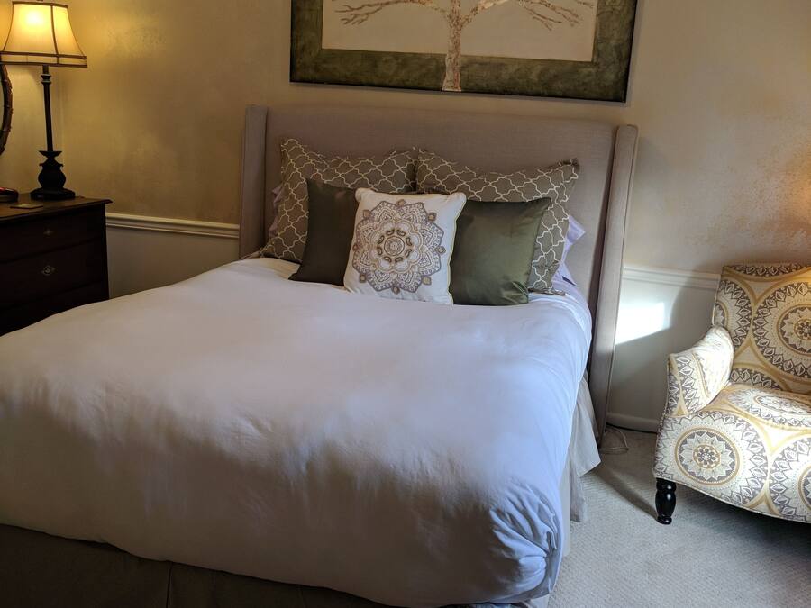 A neatly arranged bedroom with a bed, a chair, a lamp, and a ceiling fan.