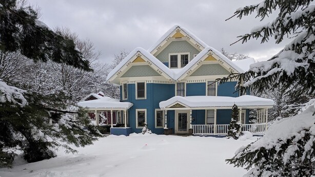 Une grande maison à deux étages, dont le toit est recouvert de neige et qui possède un porche à l’avant.