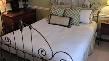 Una cama bien tendida con estructura metálica, una mesita de noche con lámpara, un aparador y un cuadro decorativo en la pared.