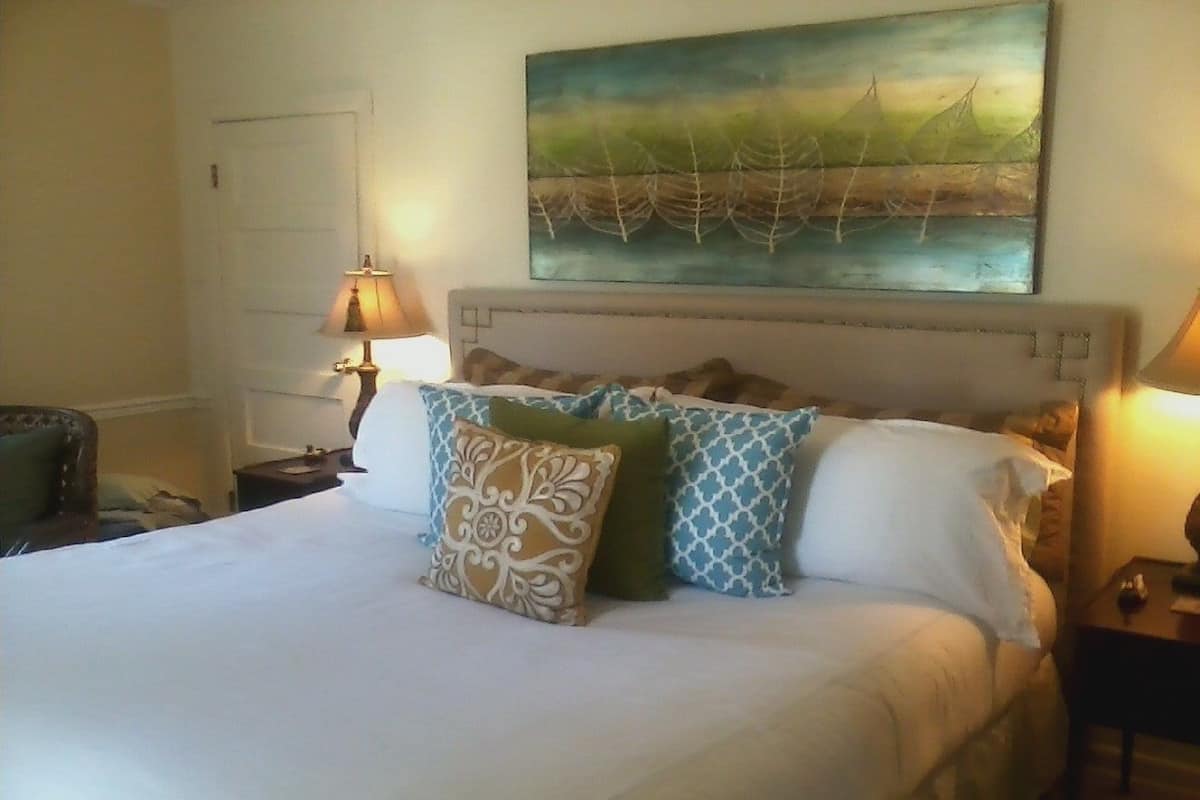 A neatly made bed with patterned pillows, a painting above it, and two bedside lamps.