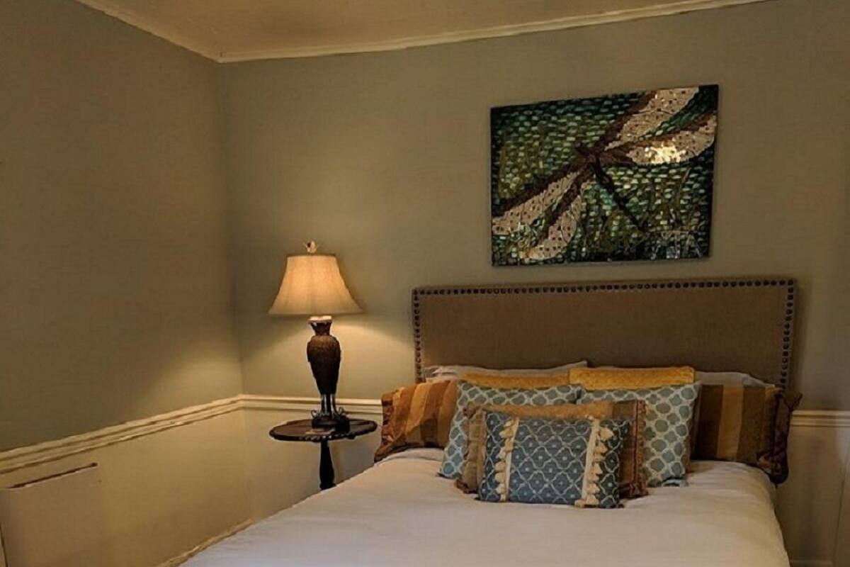 A bedroom with a large bed, a nightstand with a lamp, and a painting on the wall.