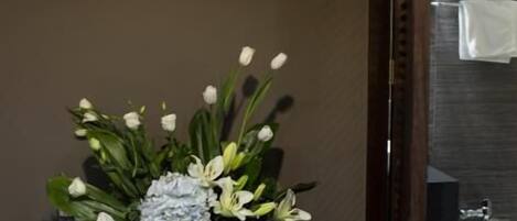 A bathroom with a toilet, a sink, and a mirror. There is a flower arrangement on a table next to the mirror.