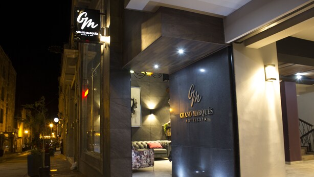 A hotel entrance with a dark facade, a visible reception area, and a staircase to the right.