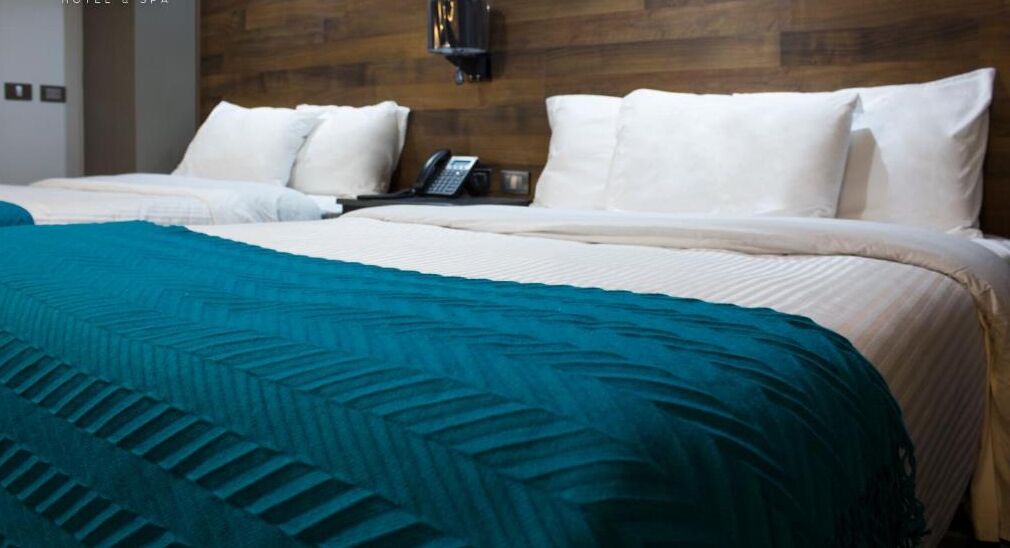 A hotel room with a wooden headboard, a bed with white bedding, a teal throw blanket, and a telephone on the nightstand.