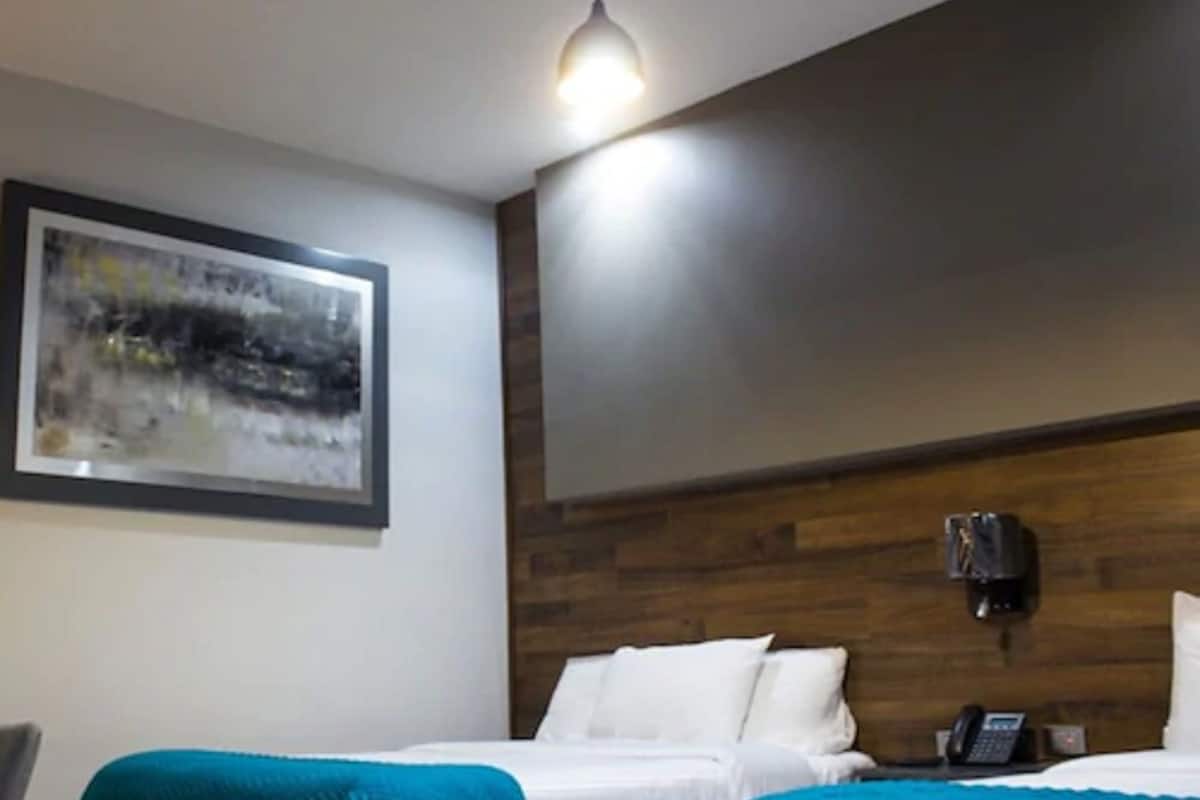 Habitación de hotel con dos camas, cabecera de madera, un cuadro en la pared y un teléfono en la mesita de noche.