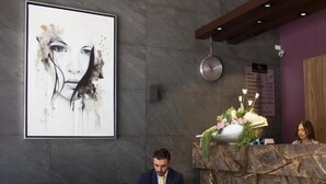 A man sitting on a dark blue leather couch in a modern lobby with a marble reception desk and a large abstract painting on the wall.