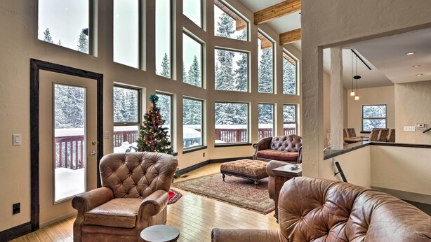 A spacious living room with large windows, leather sofas, and a Christmas tree. - Chalet Elevation (Breckenridge)