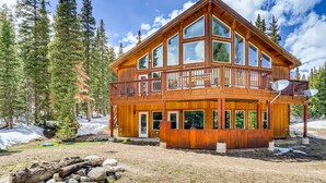 A two-story wooden cabin with large windows, a balcony, and a stone foundation. - Chalet Elevation (Breckenridge)