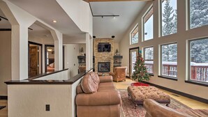A spacious living room with a stone fireplace, large windows, and a cozy seating area. - Chalet Elevation (Breckenridge)