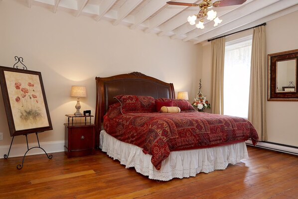 A bedroom with a wooden bed, two bedside tables, a ceiling fan, and a large mirror. - Cheltenham Suites (Caledon)