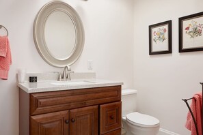 A bathroom with a white sink, wooden vanity, a white toilet, and two framed floral pictures on the wall. - Cheltenham Suites (Caledon)