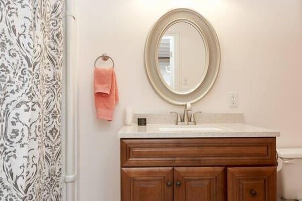 A bathroom with a wooden vanity, a round mirror, and a pink towel hanging on the wall.