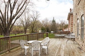 A wooden deck with outdoor furniture, a stone building, and a fenced area with trees. - Cheltenham Suites (Caledon)