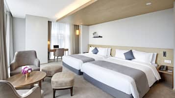 A hotel room with two beds, a desk, a chair, and a small table with flowers.