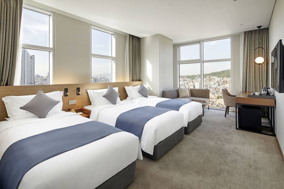Een hotelkamer met drie bedden, een bureau en een stoel.