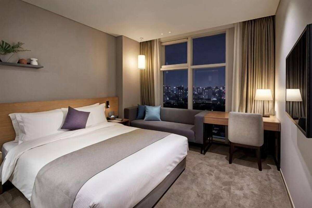 Hotelkamer met een groot bed, een bureau, een stoel, een bank en een raam met uitzicht op de stad.