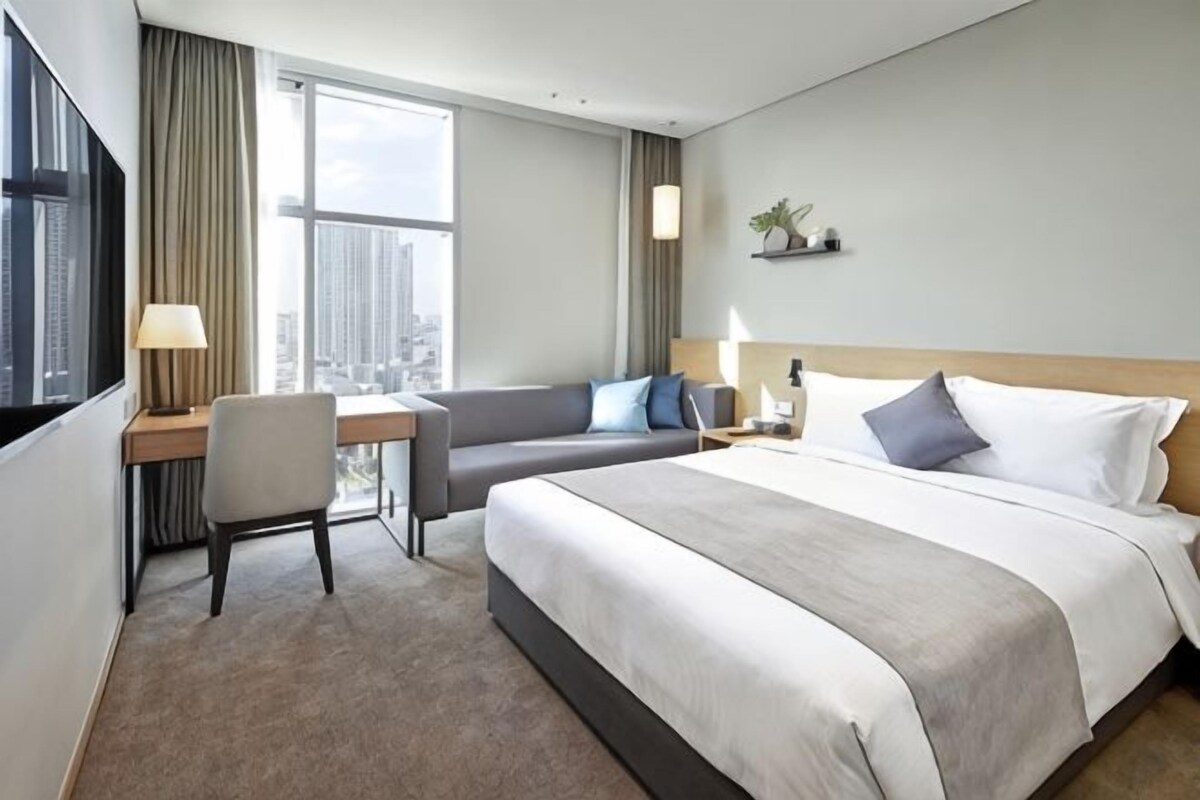 Une chambre d’hôtel équipée d’un lit, d’un bureau, d’une chaise, d’une télévision et d’une fenêtre donnant sur la ville.
