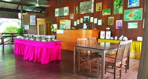 A restaurant with a wooden interior, a pink table, and various framed pictures on the walls. - Sukau Backpackers B&B (Kota Kinabatangan)