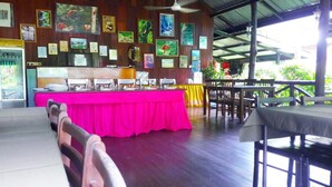 Un restaurant à l’intérieur en bois, avec un comptoir recouvert d’une nappe rose et divers tableaux encadrés accrochés aux murs.