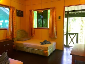 Una cama individual con cabecera, una mesita de noche, una ventana con cortinas y una puerta que da al exterior.