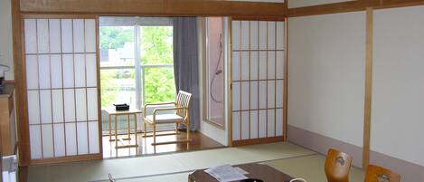 A traditional Japanese room with tatami flooring, a low table with tea set, and sliding doors leading to an outdoor area.