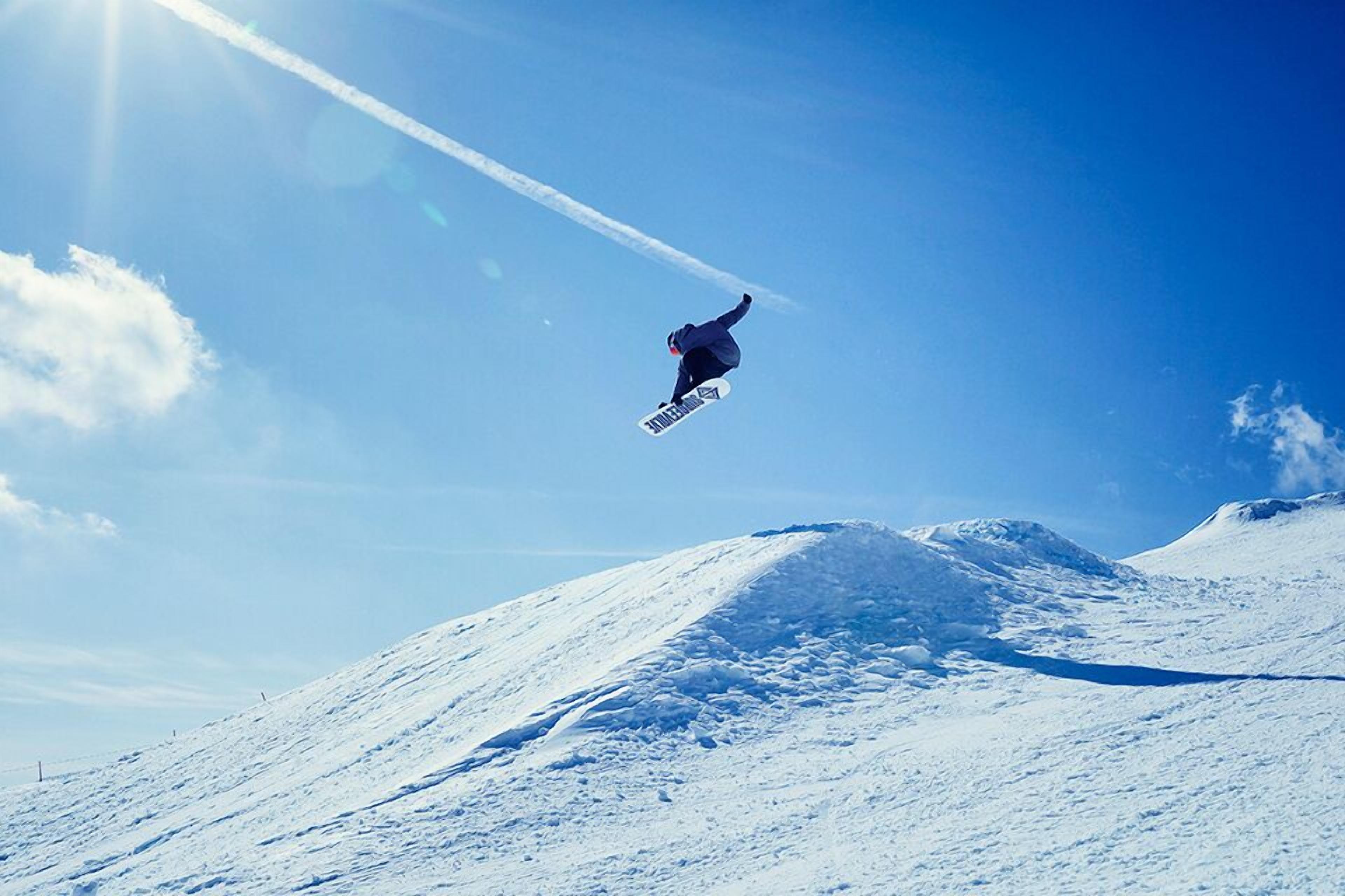 A snowboarder in mid-air against a clear blue sky.