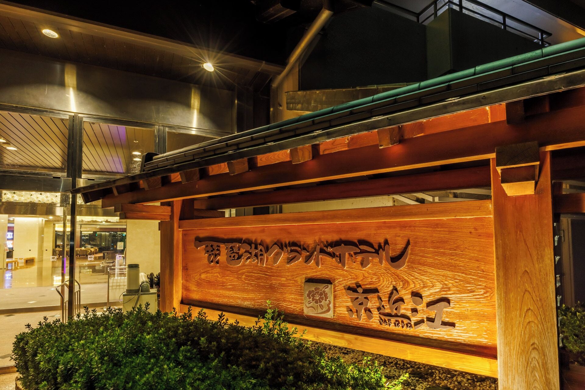 A wooden sign with Japanese characters, a metal railing, and a glass door leading to an interior space.