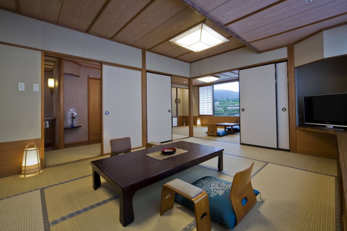 A traditional Japanese-style room with tatami flooring, a low wooden table, and a television on the right.