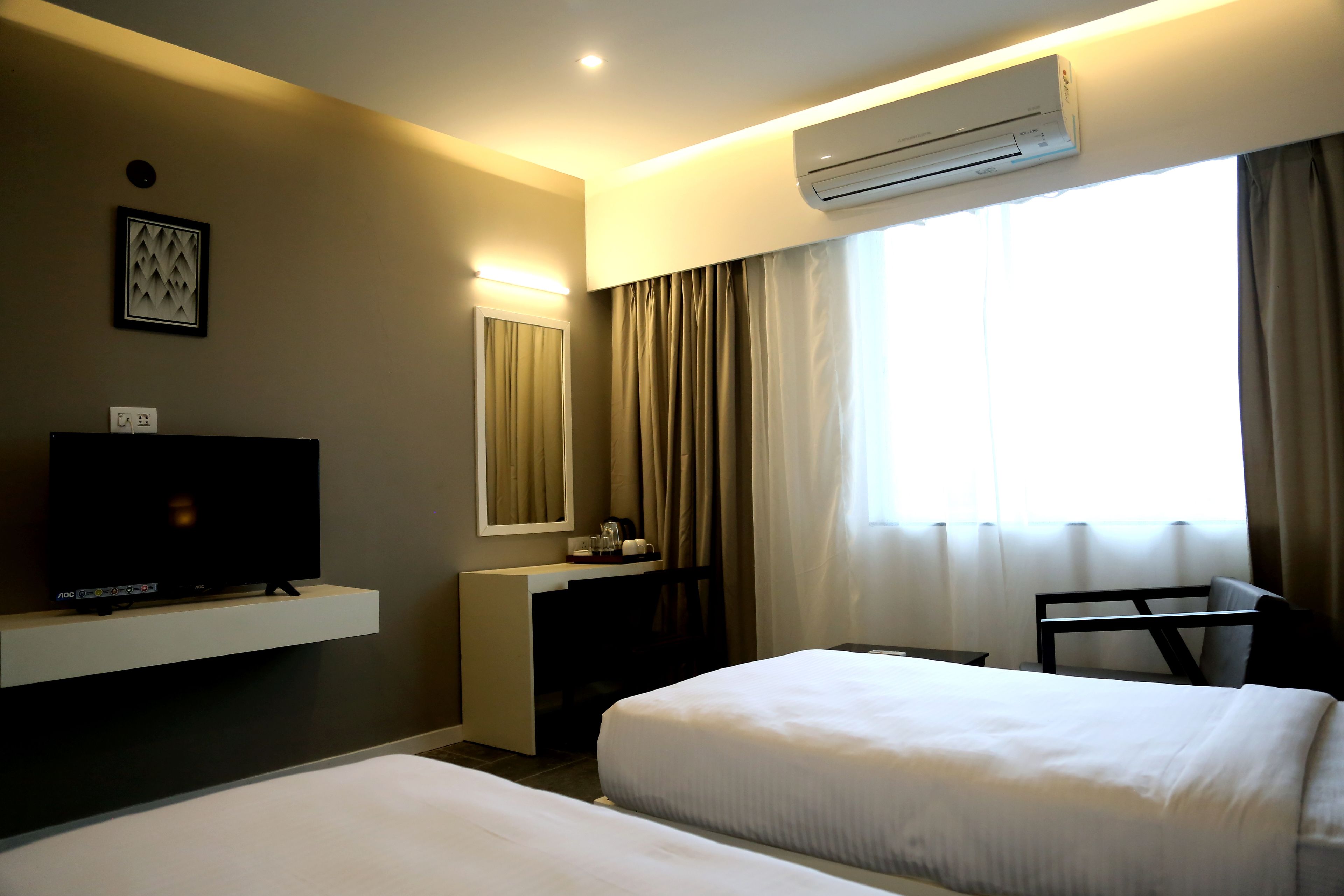 A hotel room with two beds, a TV on a stand, an air conditioner, a desk, and a window with curtains.