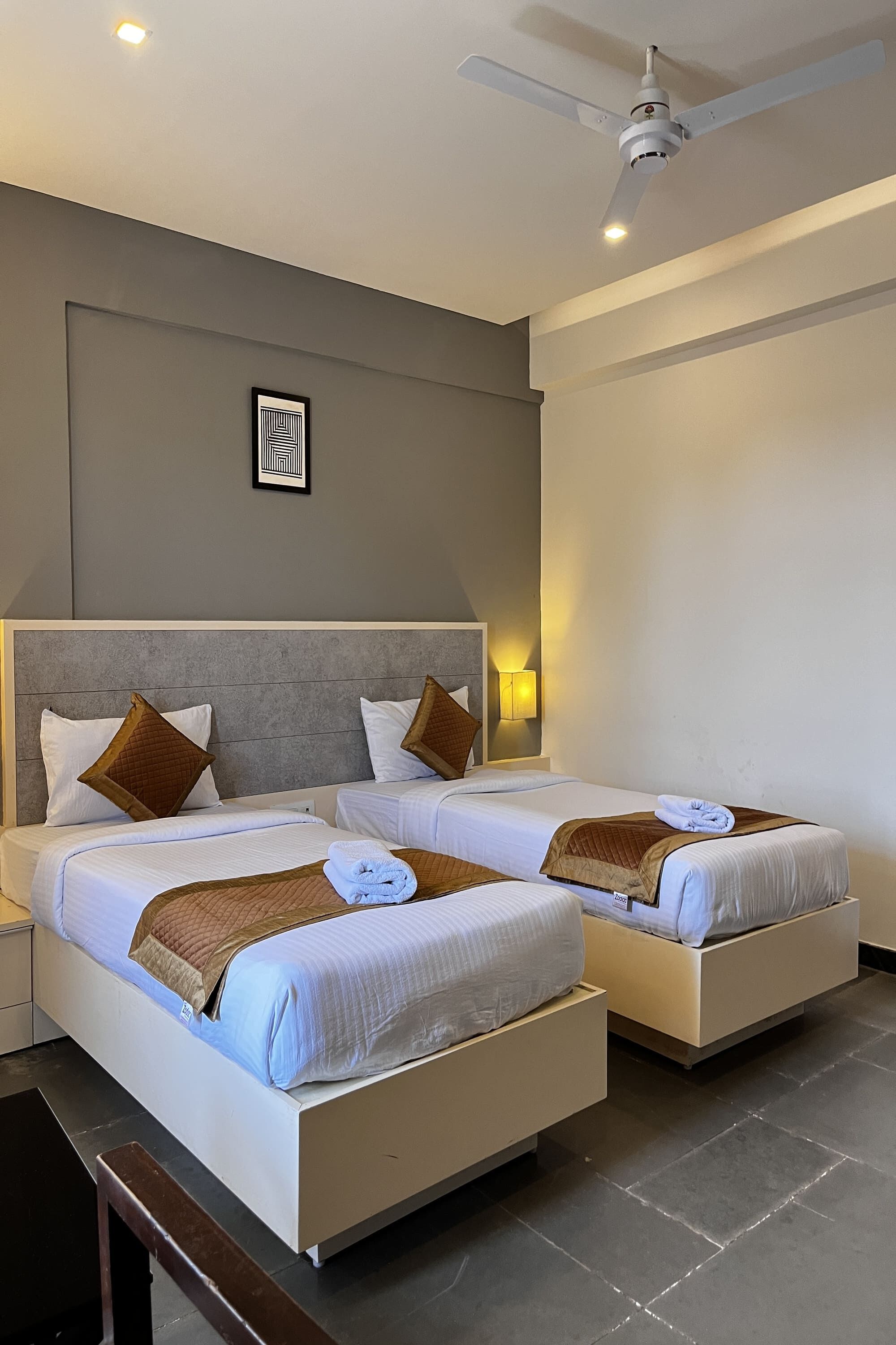 A hotel room with two beds, a ceiling fan, and a wall-mounted light fixture.
