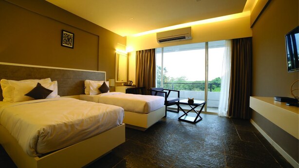 A hotel room with two beds, a small table, a chair, an air conditioning unit, a television, and a balcony with curtains. - Dwarawata Dharwad (Dharwad)