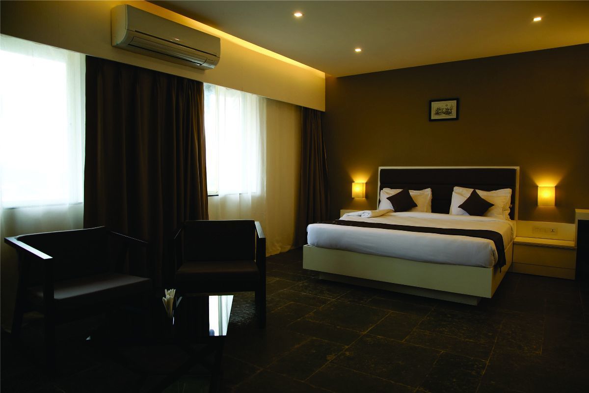 Habitación de hotel con cama, mesitas de noche, aire acondicionado, ventana con cortinas y una silla.