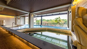 An indoor swimming pool with a tiled edge, wooden ceiling, and a view of palm trees outside.